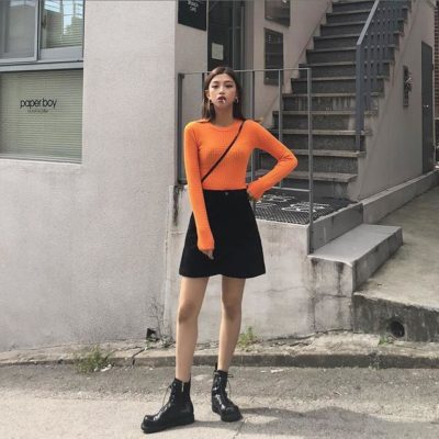 Áo thun gân tone cam sáng và chân váy đen và boot cao cổ